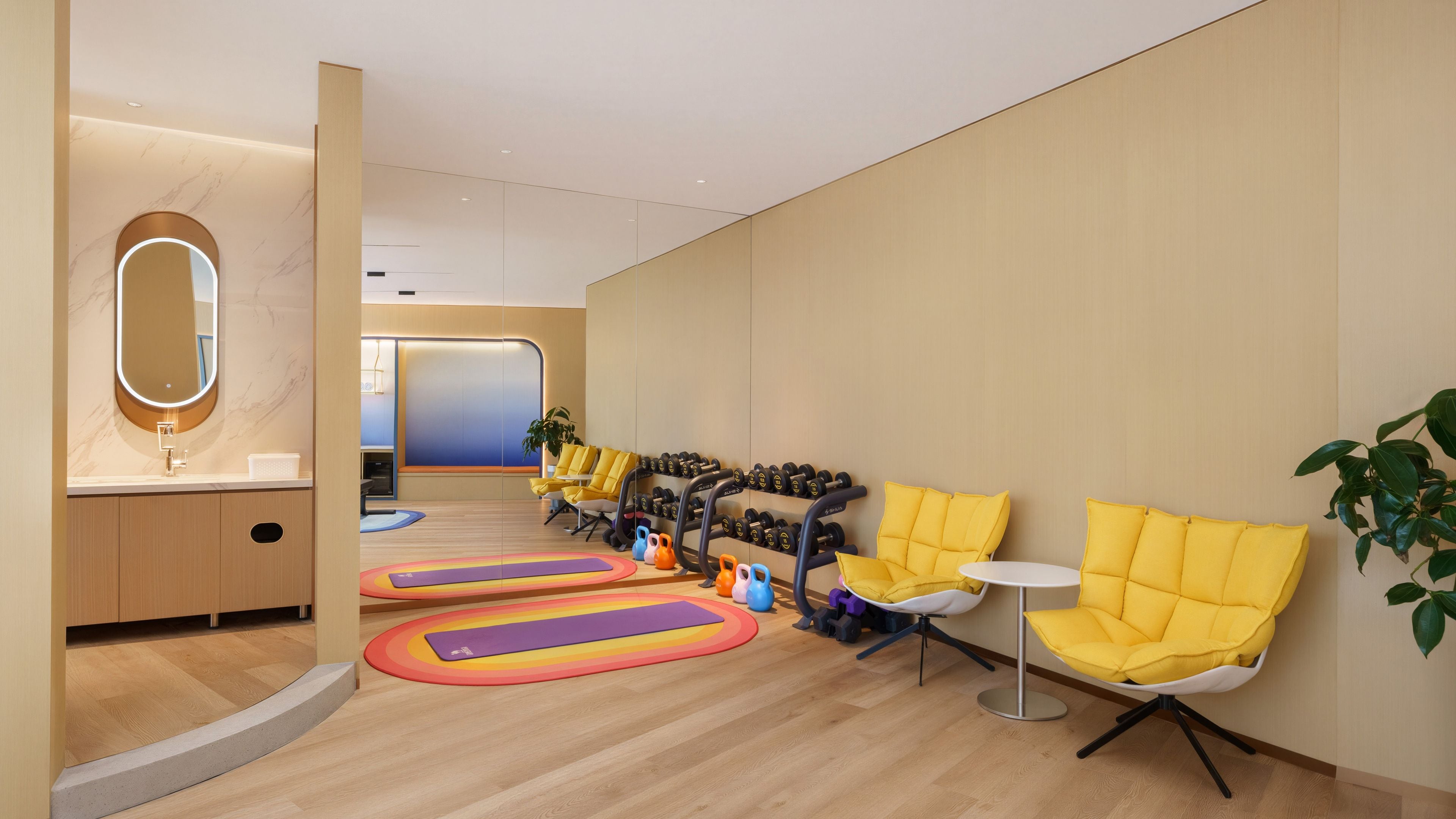 Un espace d’attente moderne comprenant un comptoir d’accueil, un miroir, des chaises jaunes et du matériel d’exercice.