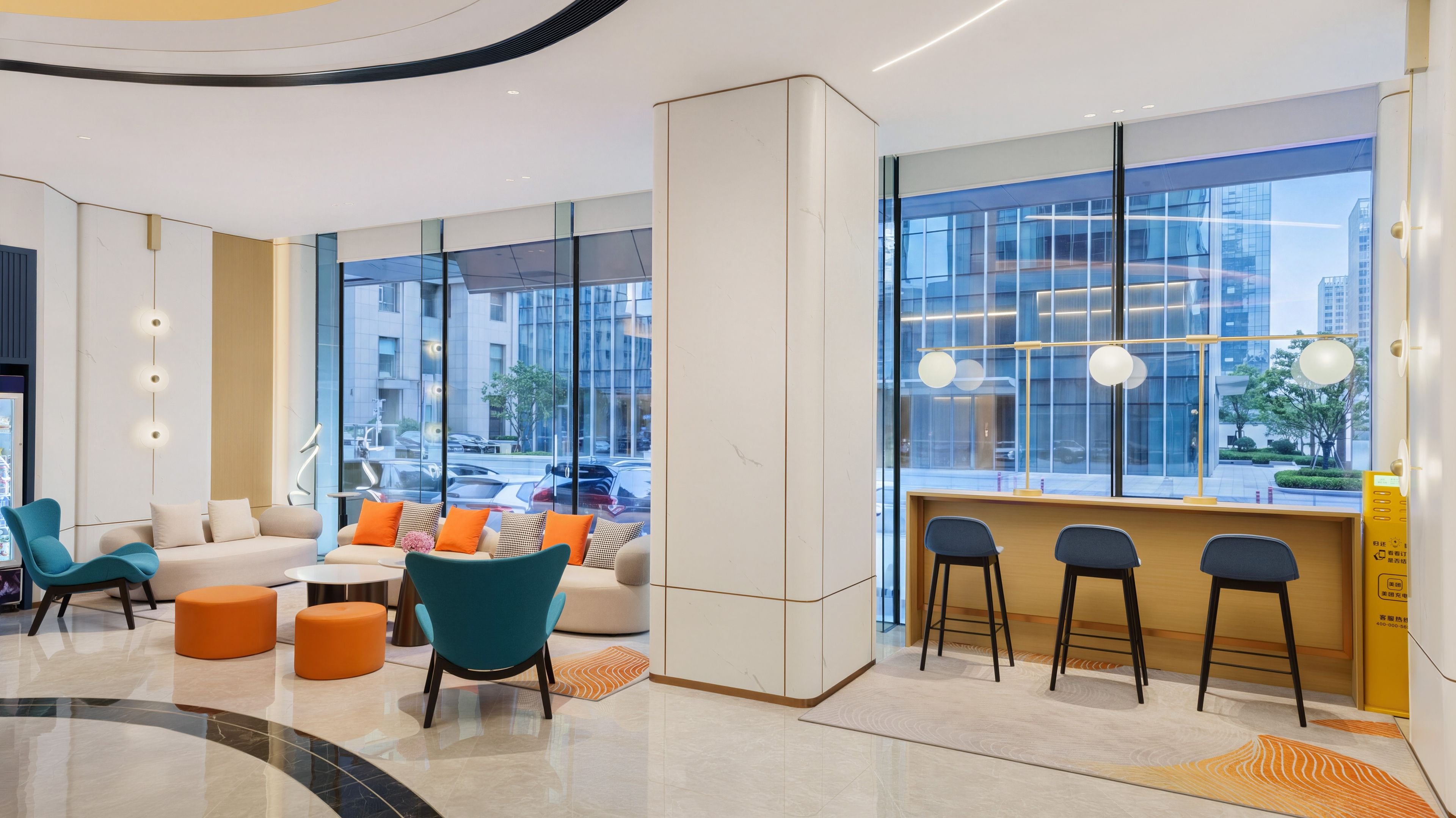A modern hotel lobby with a seating area, a reception desk, and large windows offering city views.