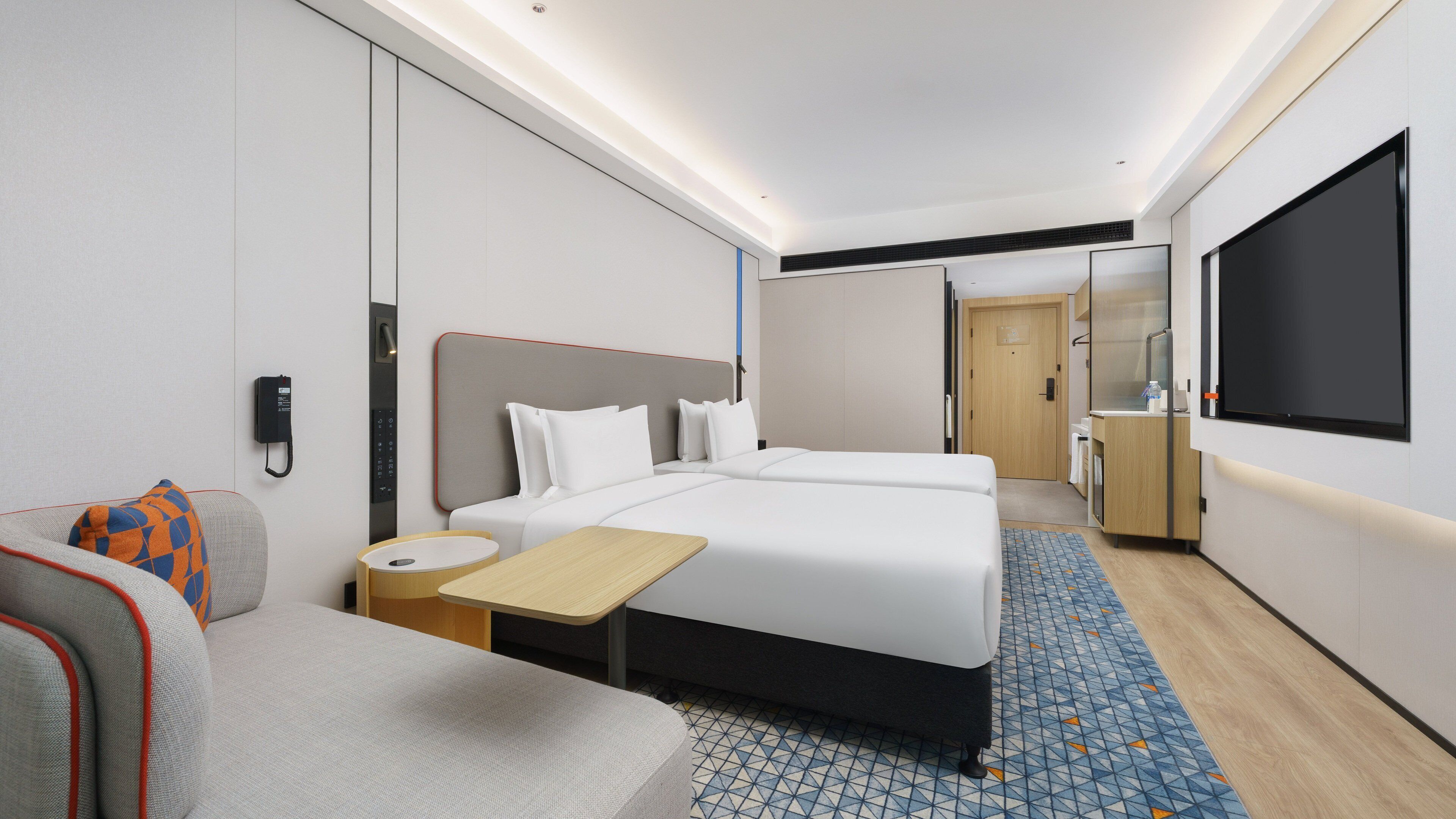 Quarto de hotel com cama, escrivaninha, cadeira, televisão e banheiro.