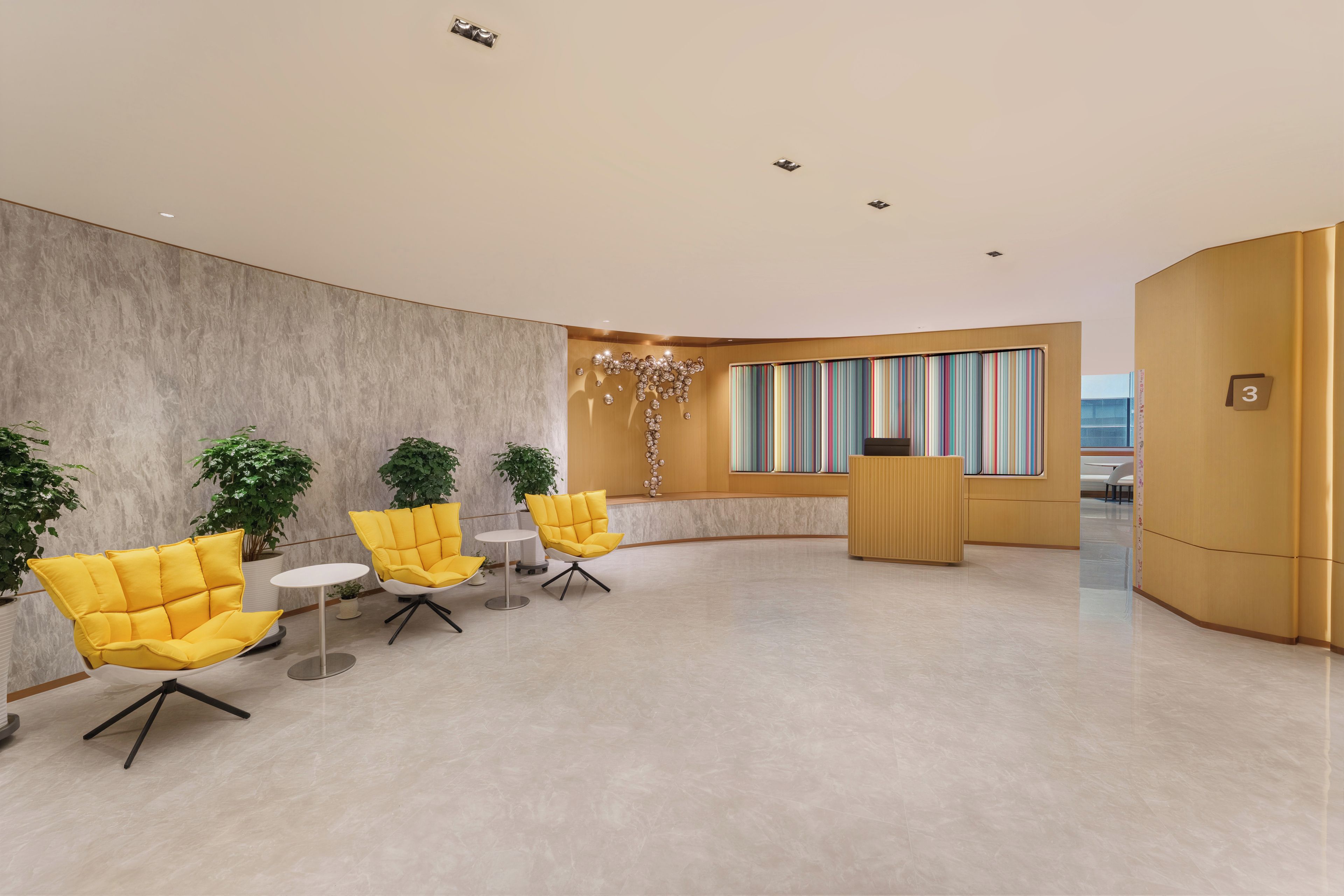 A modern lobby with a marble floor, yellow chairs, a reception desk, and a large window with colorful curtains.