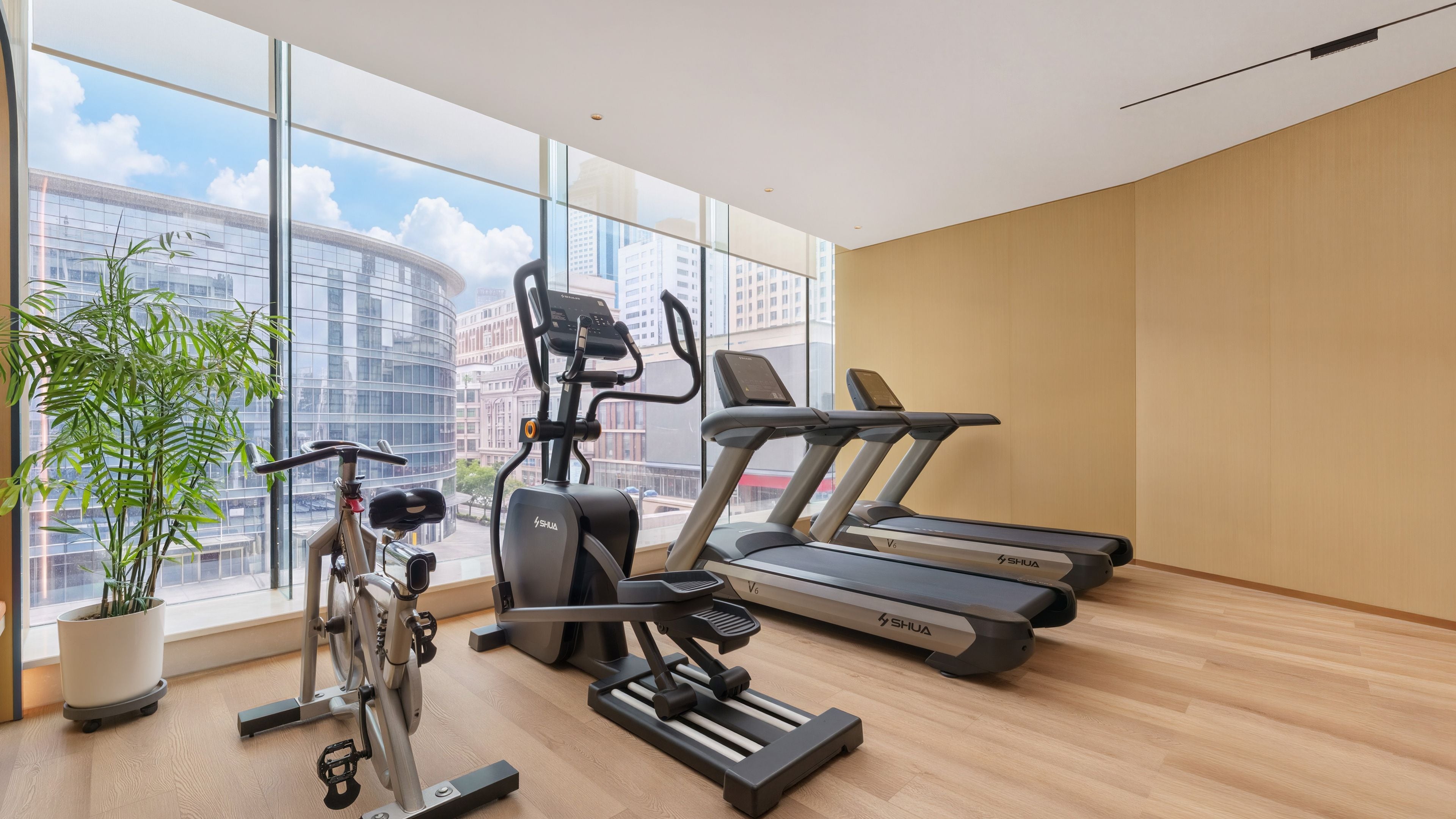 A gym with exercise equipment, large windows, and a view of buildings.