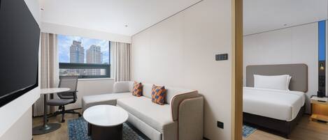 A hotel room with a sofa, a bed, a desk, and a TV.