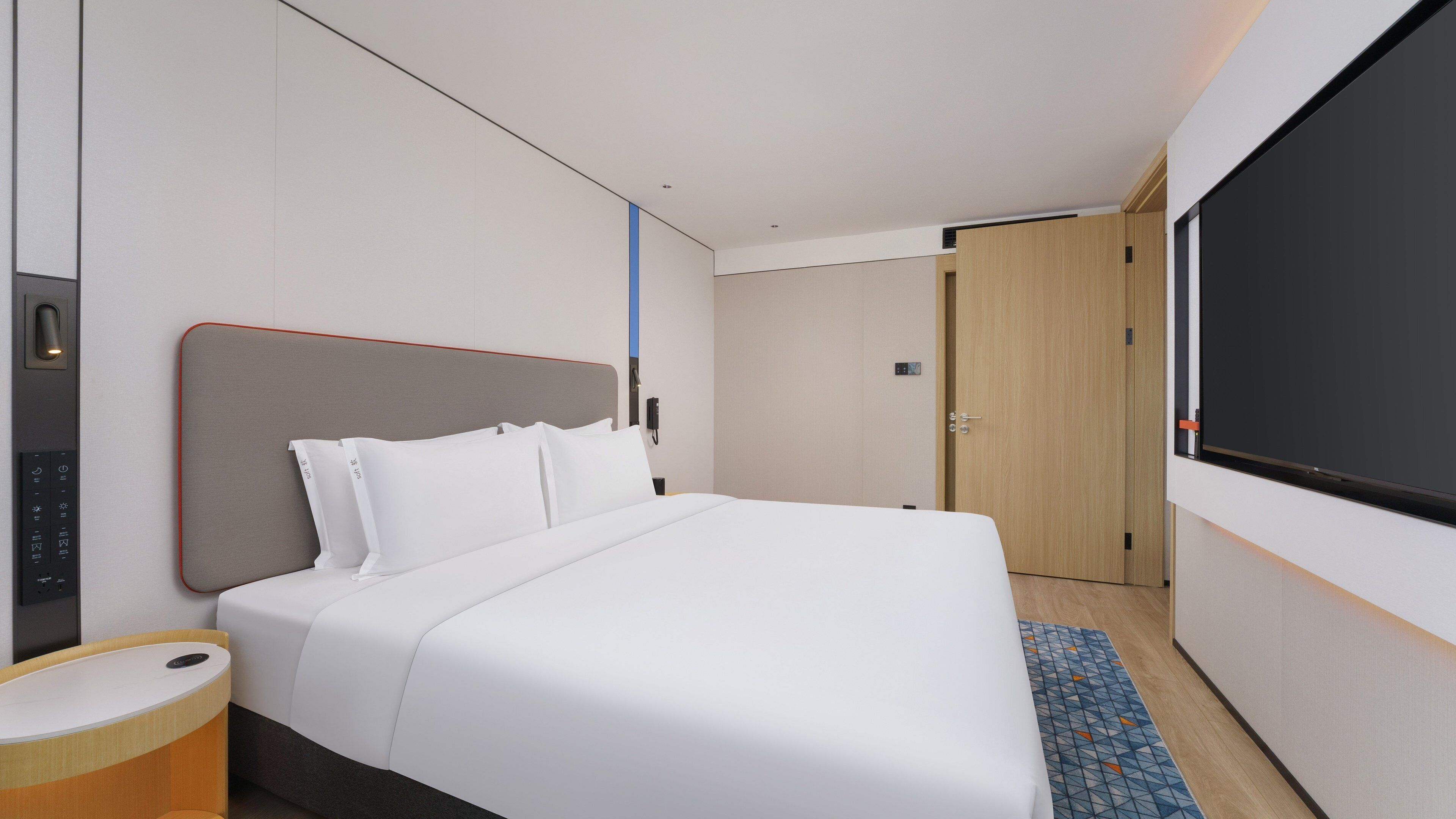 A hotel room with a bed, a bedside table, a TV, and a door.