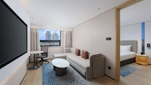 A modern hotel room with a sofa, a small table, a bed, and a large window offering a city view. - Holiday Inn Express Dalian City Centre by IHG (Dalian)