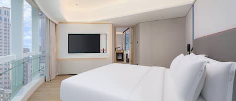 A hotel room with a large bed, a flat-screen TV mounted on the wall, and a view of the city through large windows.