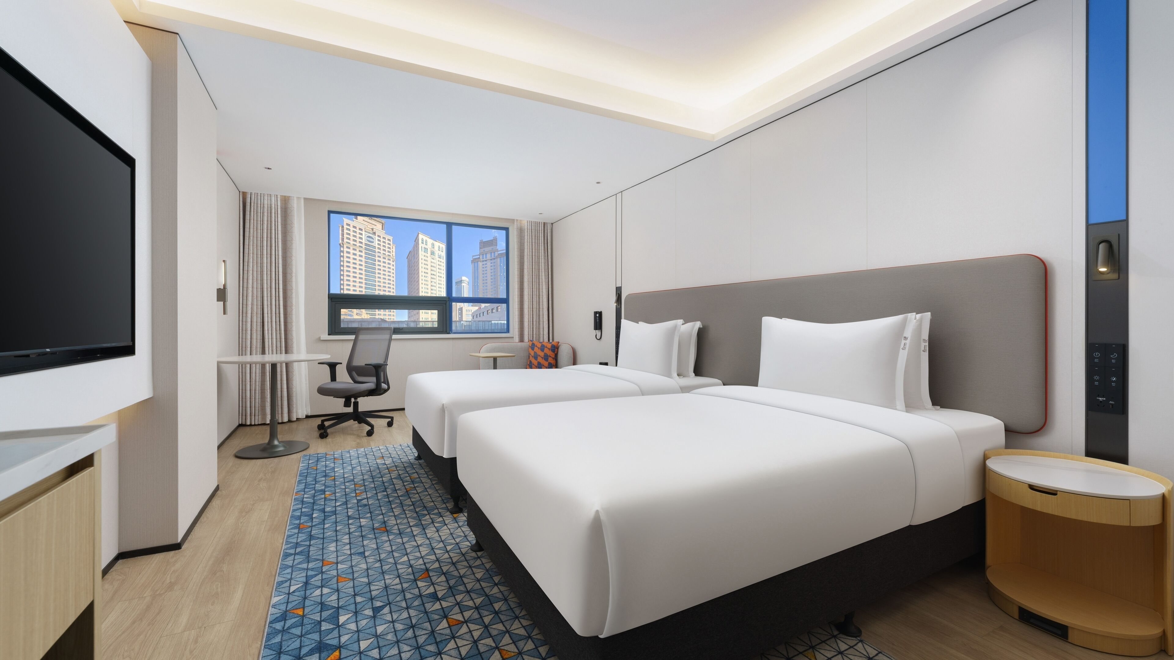 Une chambre d’hôtel avec deux lits, un bureau, une télévision et une fenêtre donnant sur la ville.