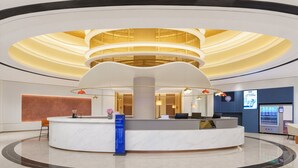 A modern hotel lobby with a central reception desk, seating area, and a large digital screen displaying information. - Holiday Inn Express Dalian City Centre by IHG (Dalian)