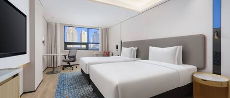 A hotel room with two beds, a desk, a TV, and a window with a city view.