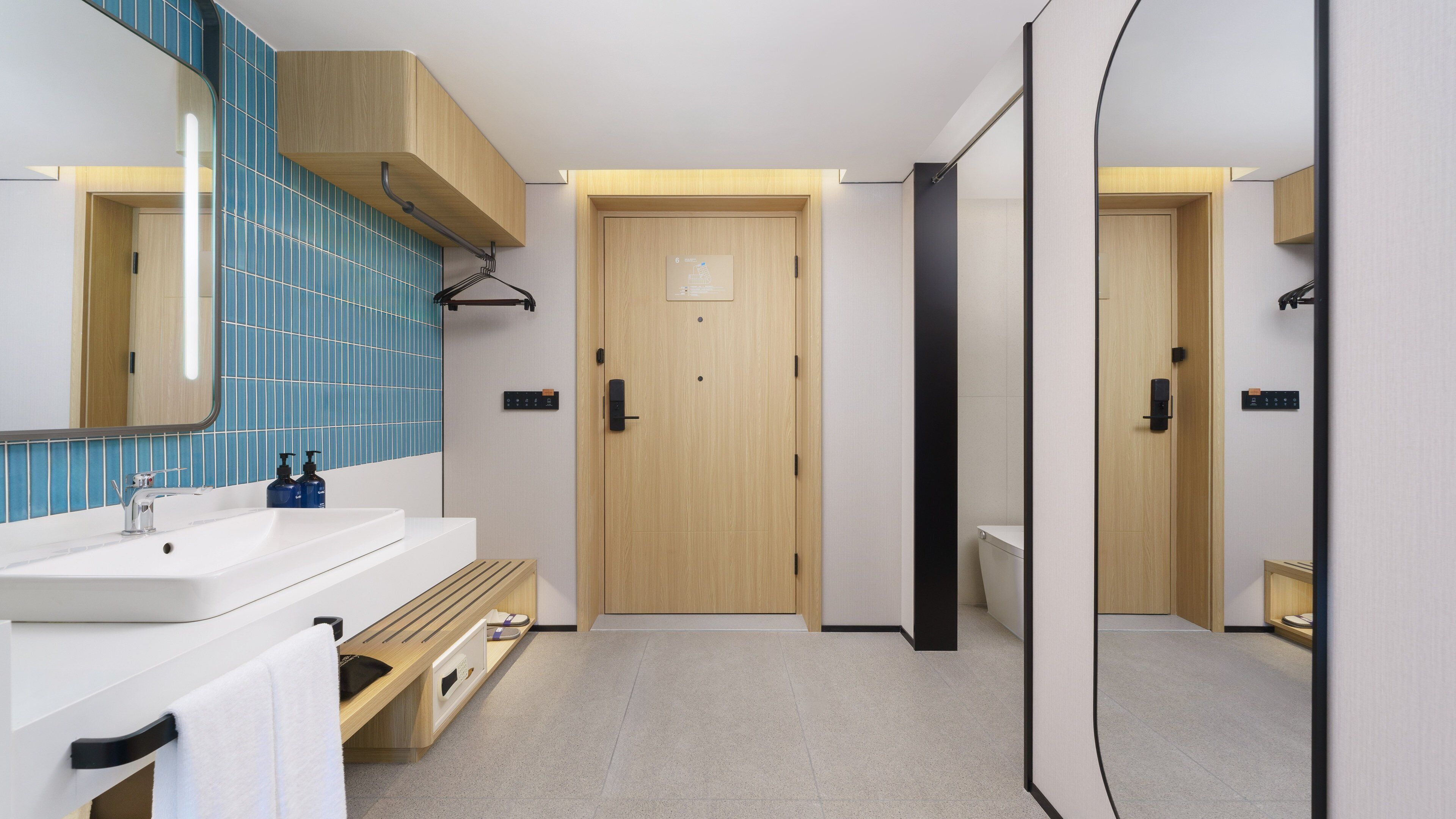 Un baño moderno con un lavamanos blanco, pared con azulejos azules, puerta de madera y un espejo.