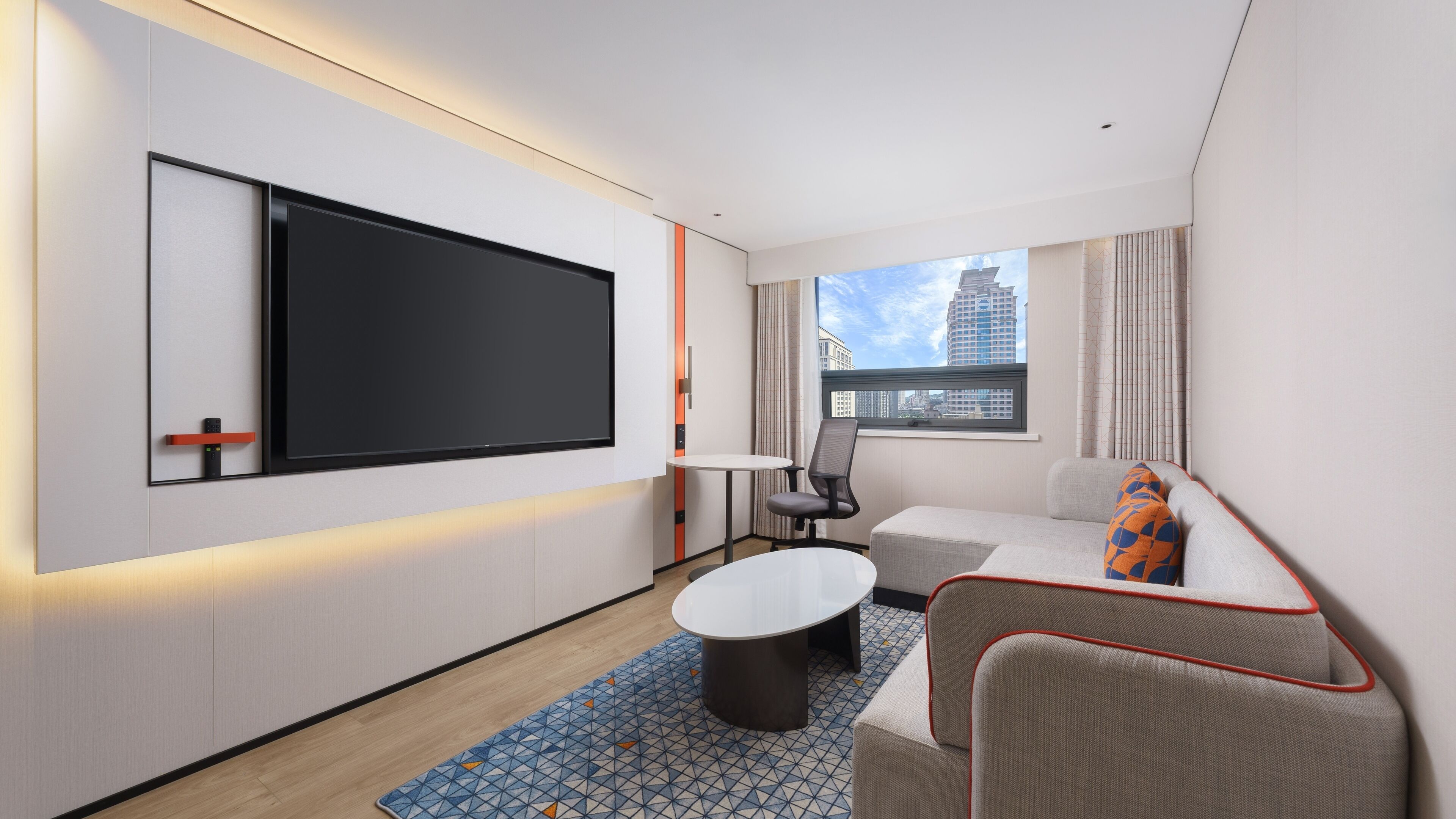 A modern hotel room with a flat-screen TV, a sofa, a small table, and a patterned rug.