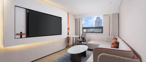 A modern hotel room with a flat-screen TV, a sofa, a small table, and a patterned rug.