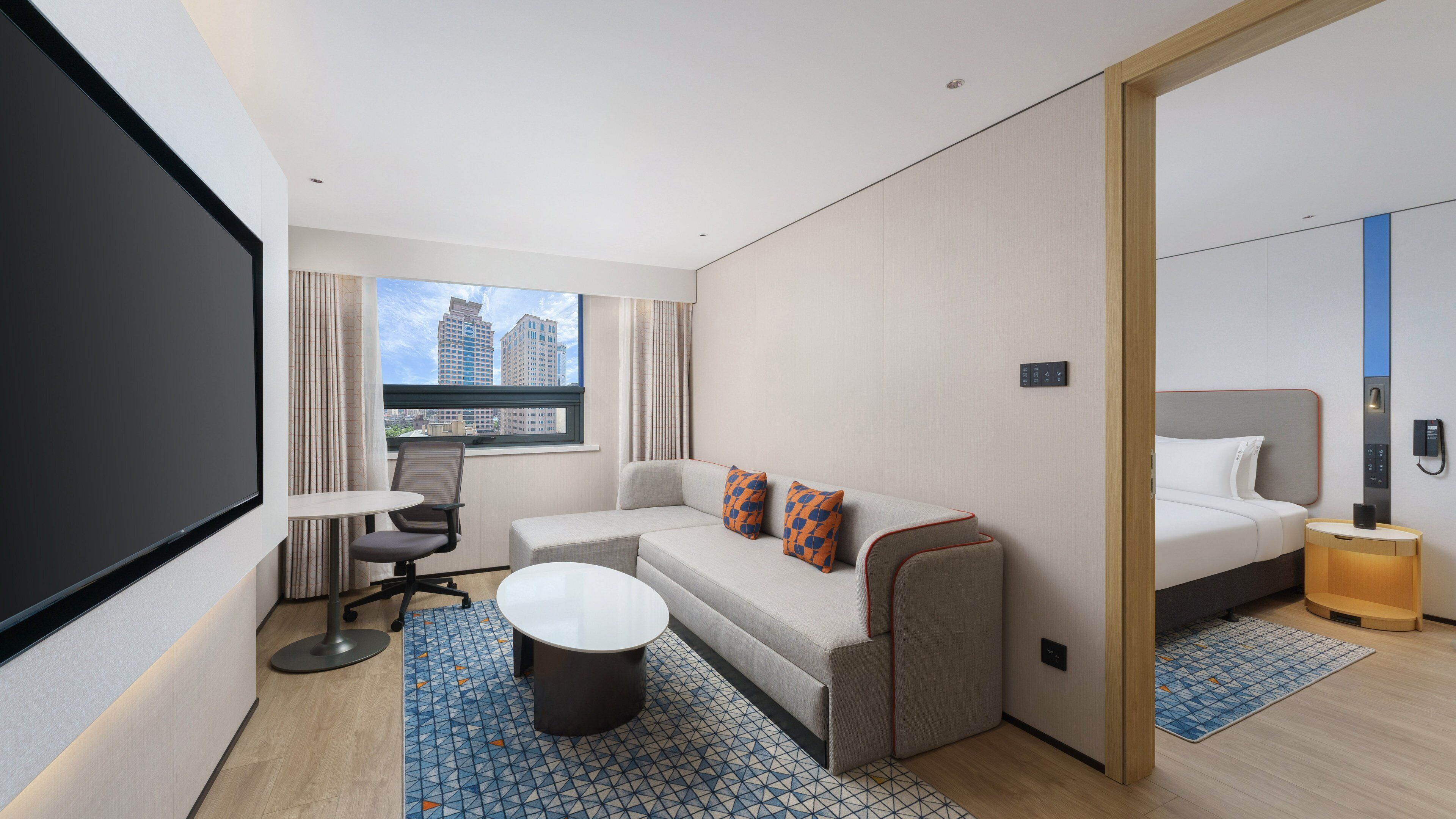Une chambre d’hôtel moderne équipée d’un canapé, d’une petite table, d’un lit et d’une grande fenêtre donnant sur la ville.