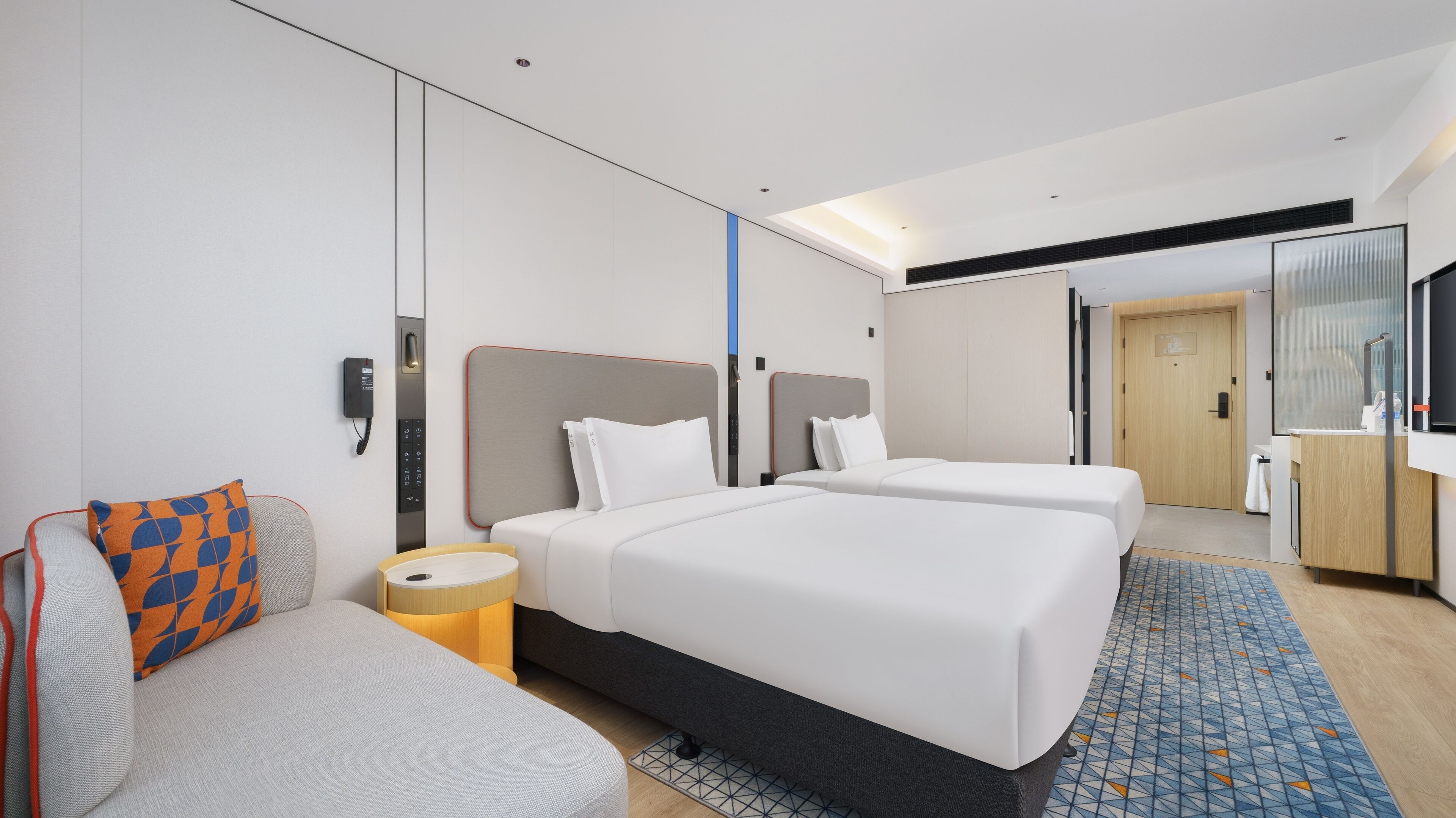 Une chambre d’hôtel moderne avec deux lits, un canapé, une petite table et un téléviseur.