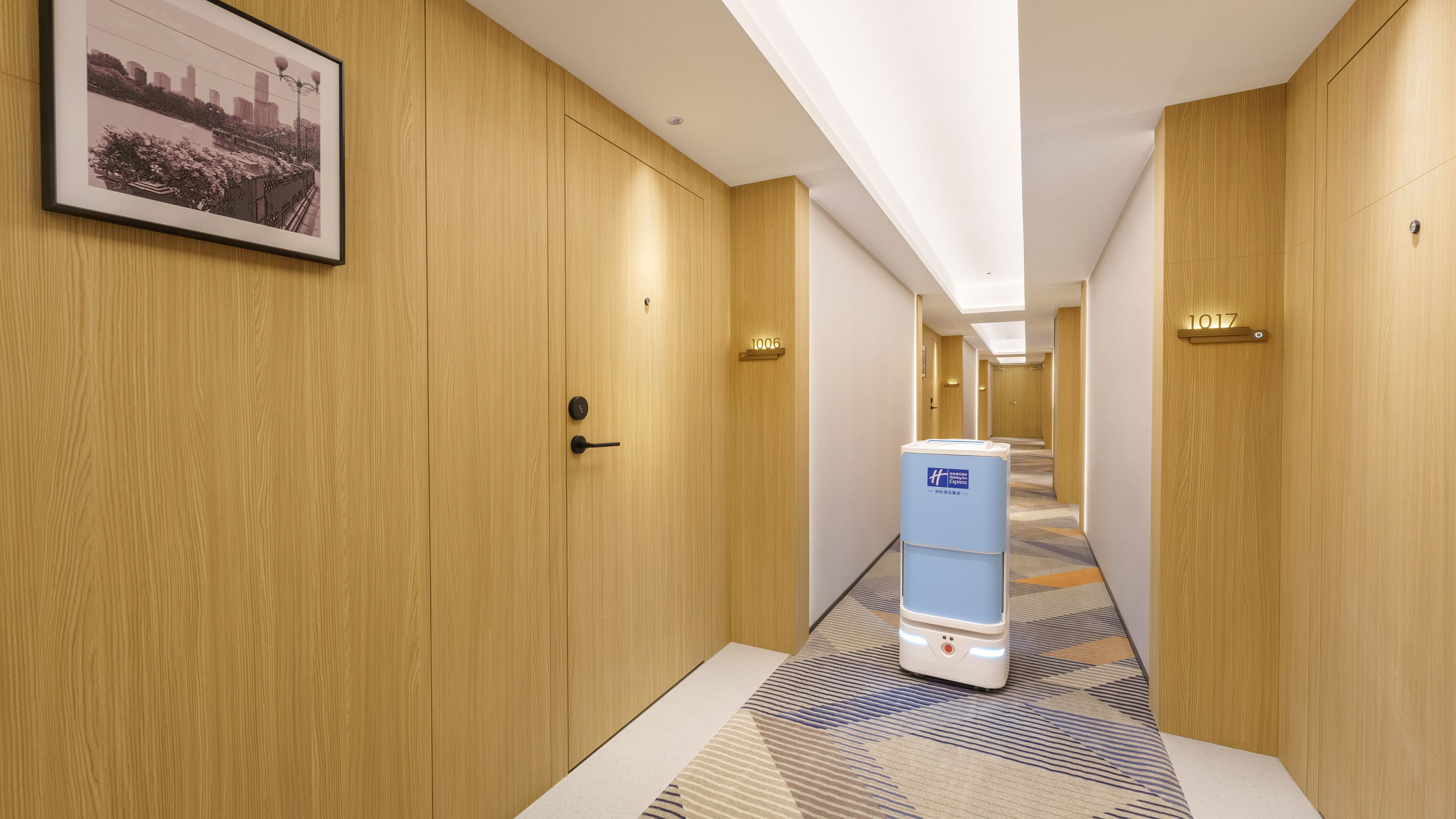 Un couloir d’hôtel avec des portes en bois, un distributeur d’eau et un tableau encadré au mur.