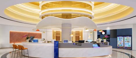 En moderne hotellobby med en central receptionsdisk, siddeområde og et stort, cirkulært loftsdesign.