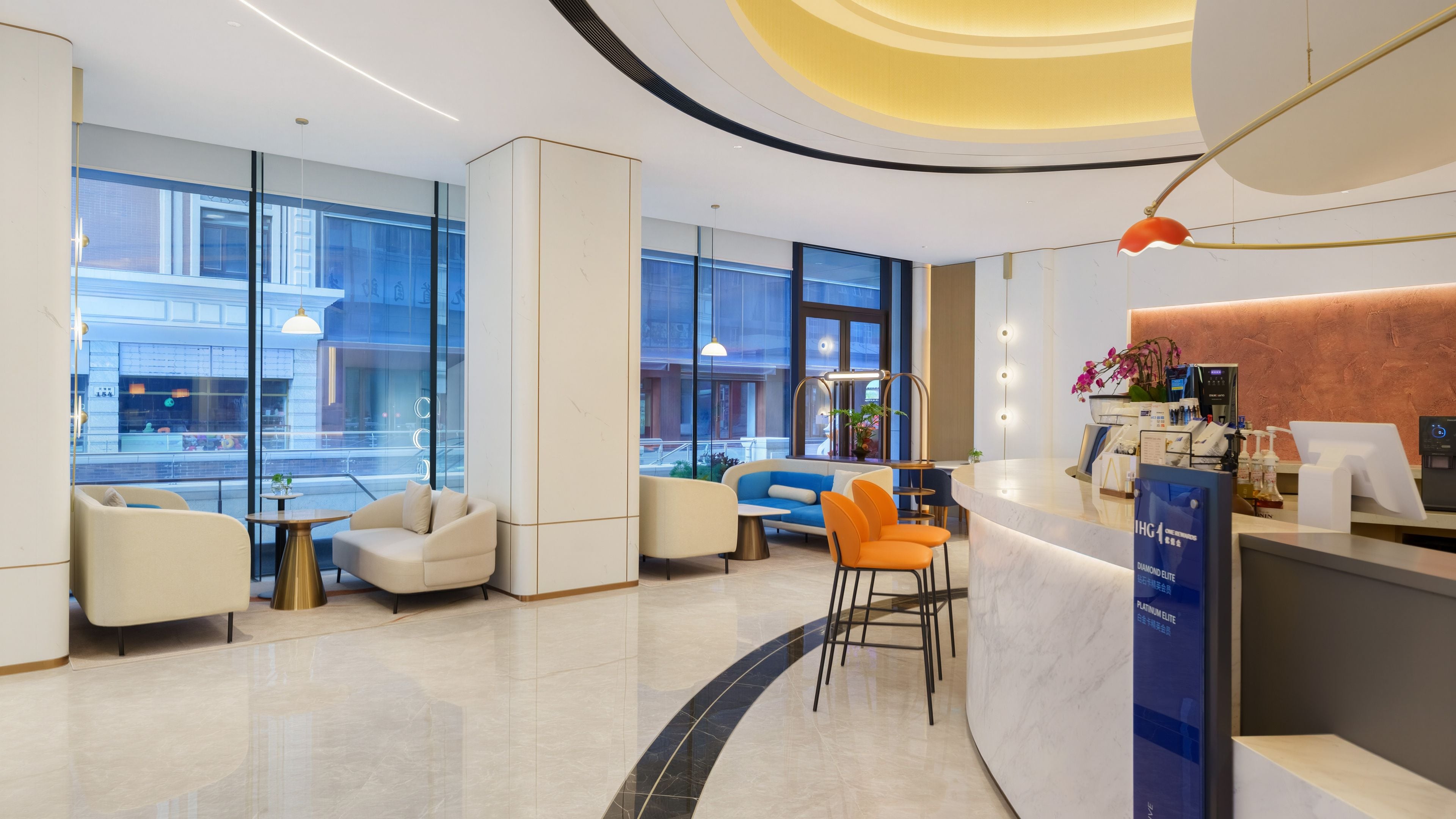 A modern hotel lobby with seating areas, a reception desk, and large windows offering views of the street.
