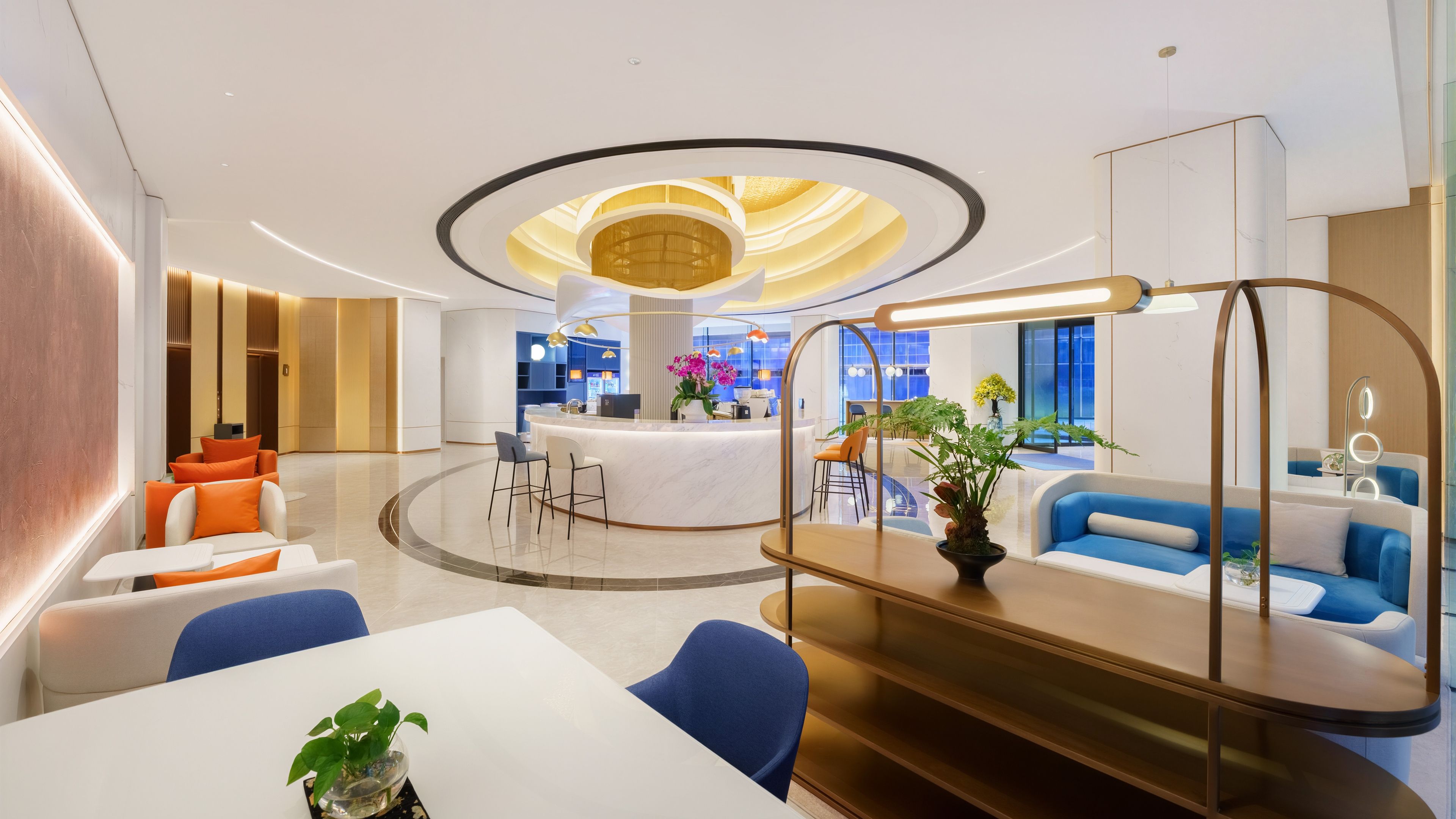 Un hall d’hôtel moderne avec un comptoir d’accueil central, des espaces de détente et un plafond au design circulaire.