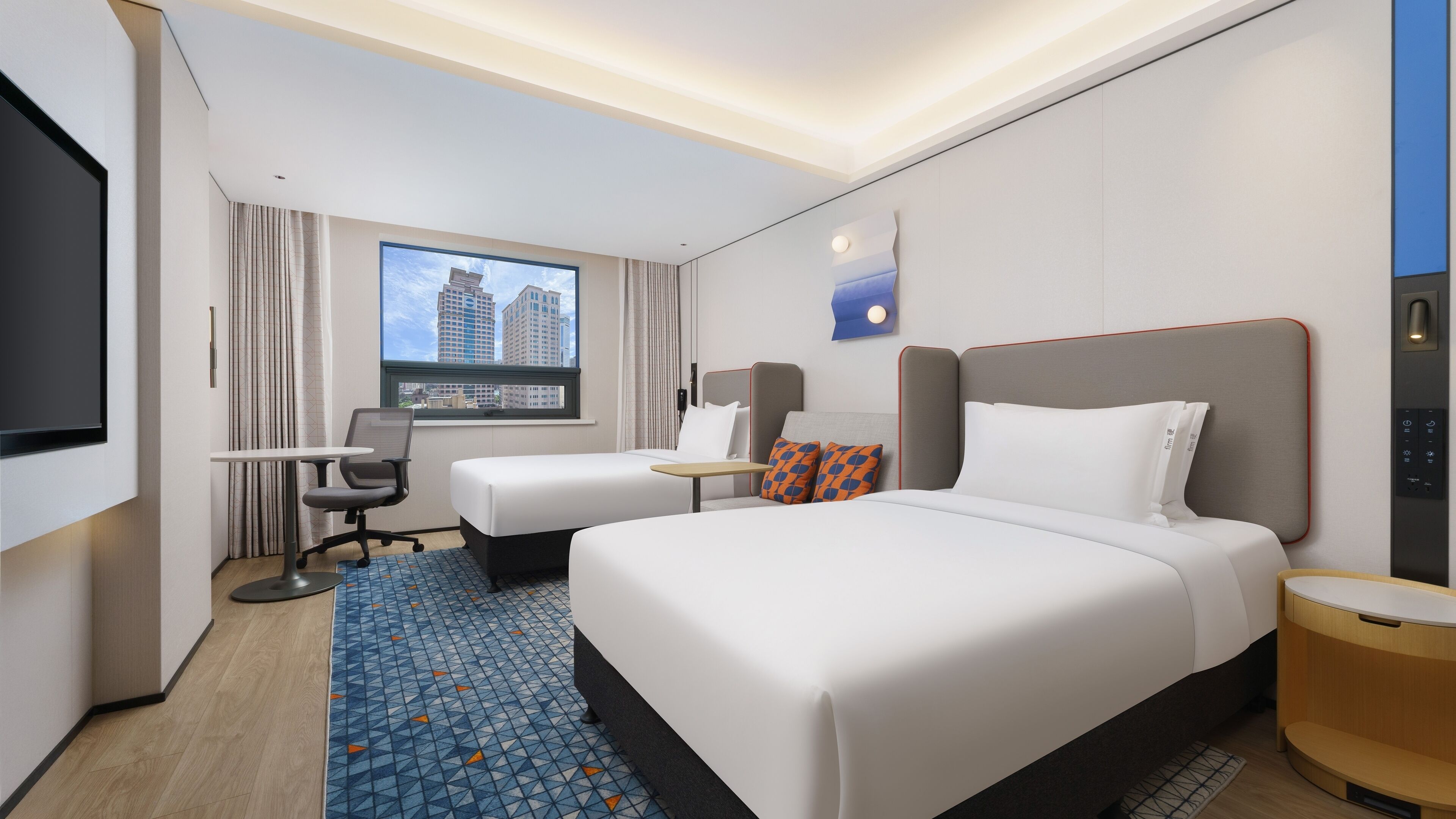A hotel room with a large bed, a desk, a chair, a TV, and a window with a city view.