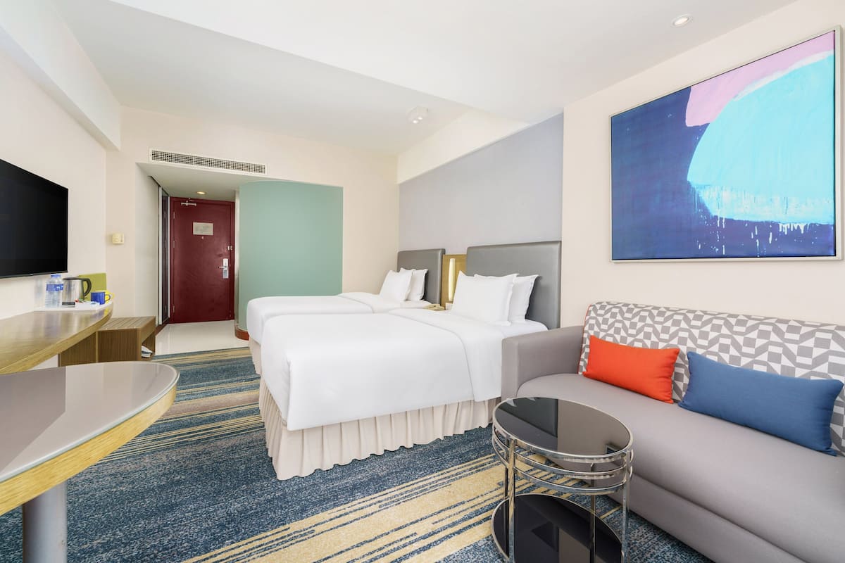 A hotel room with a bed, a sofa, a TV, and a painting on the wall.