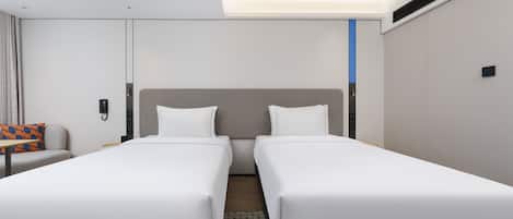 A hotel room with two single beds, a sofa, a small table, and a wall-mounted phone.