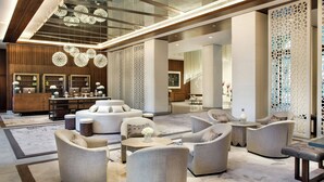 Een ruime lobby met een modern design, met een centraal zithoek met banken en fauteuils, een receptiebalie en decoratieve verlichting.