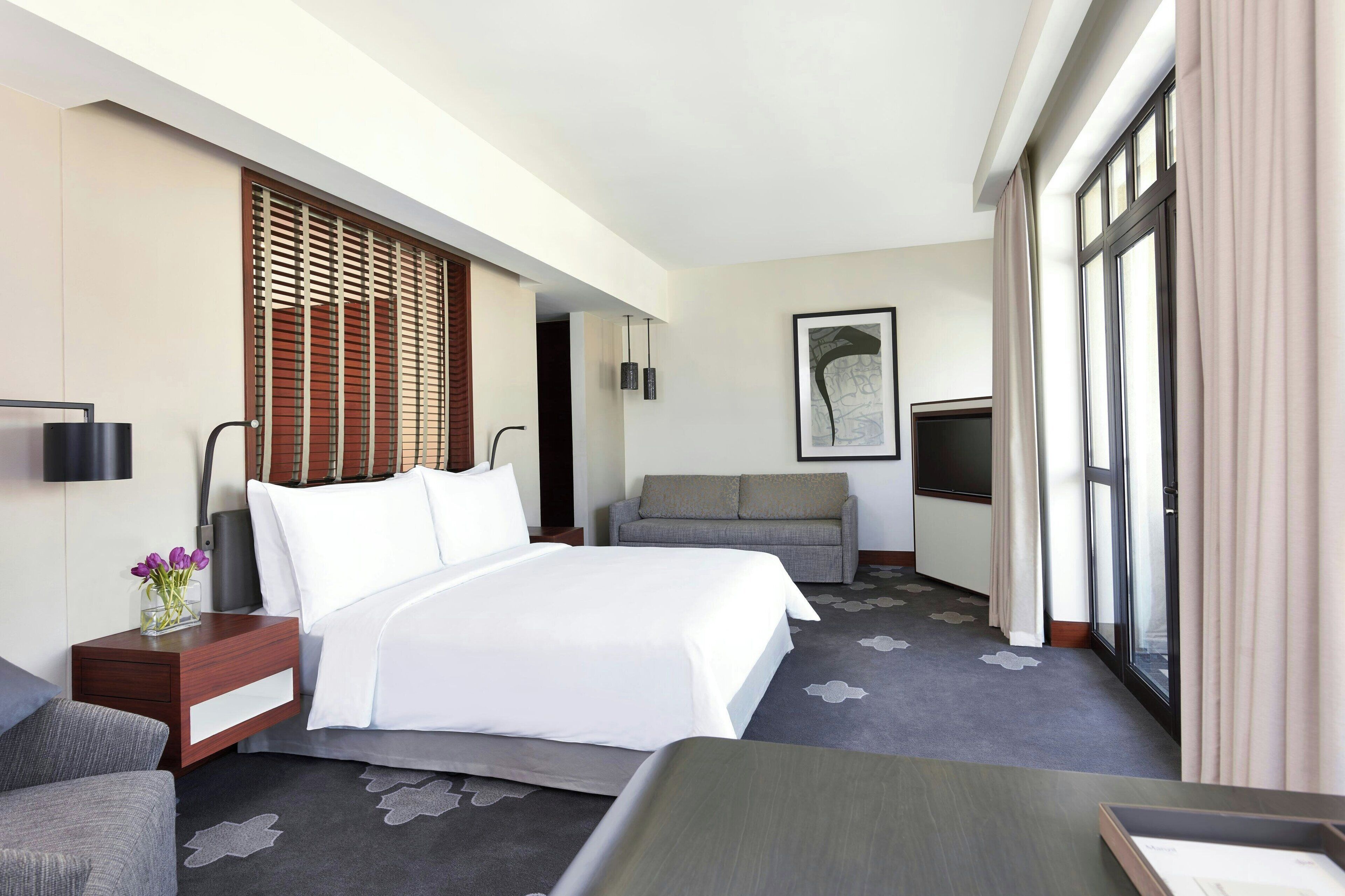 A hotel room with a bed, a sofa, a desk, a TV, and a window with curtains.