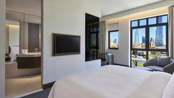 A hotel room with a large bed, a TV, a desk with a chair, a bathroom, and a city view.