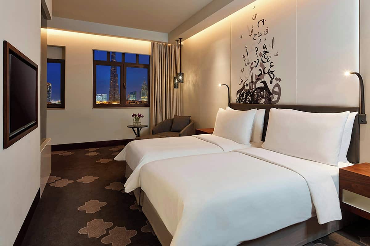 A hotel room with two beds, a TV, a city view, and a decorative wall piece.