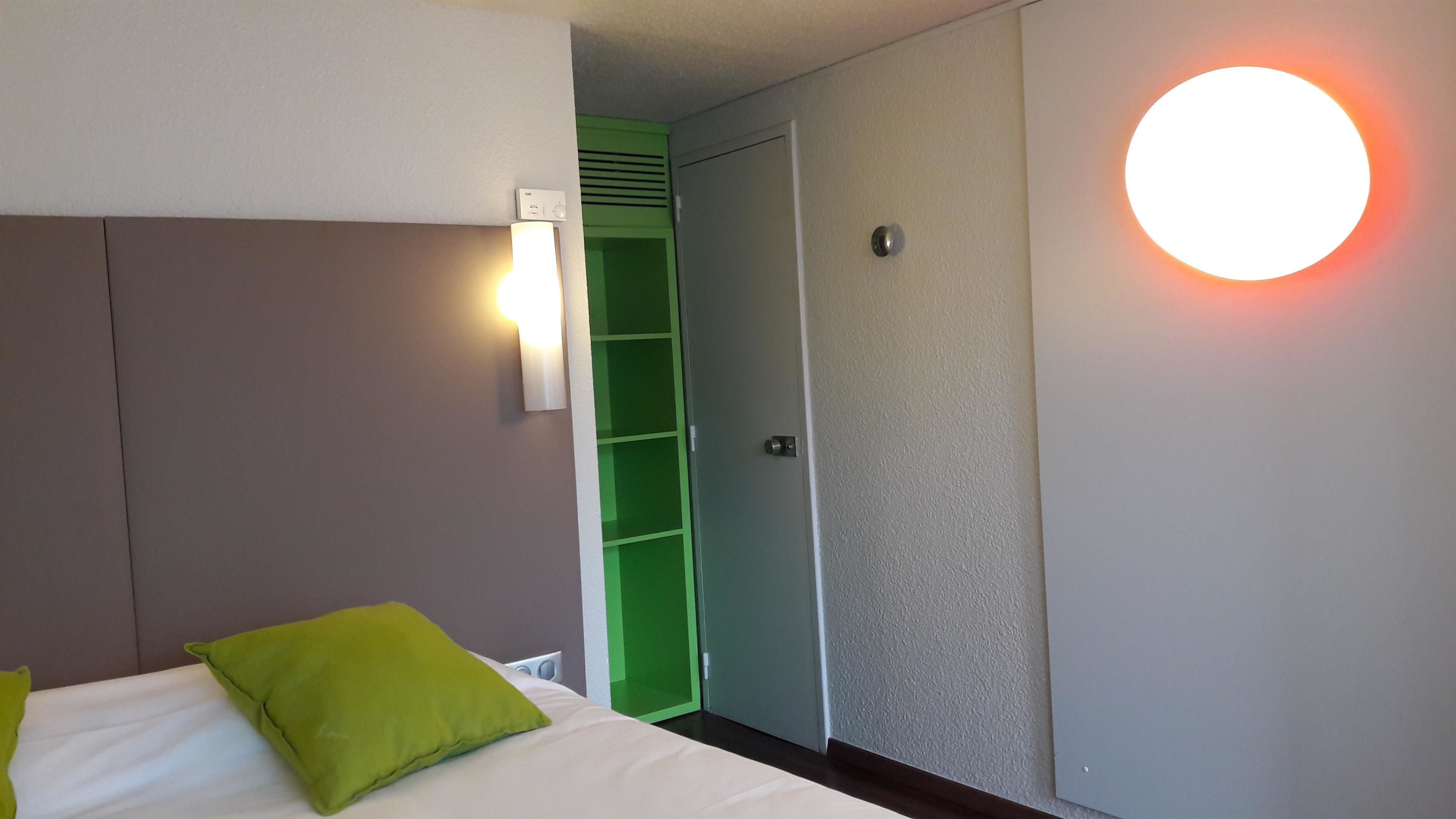 A hotel room with a bed, a green wall, a wardrobe, and a circular light fixture.