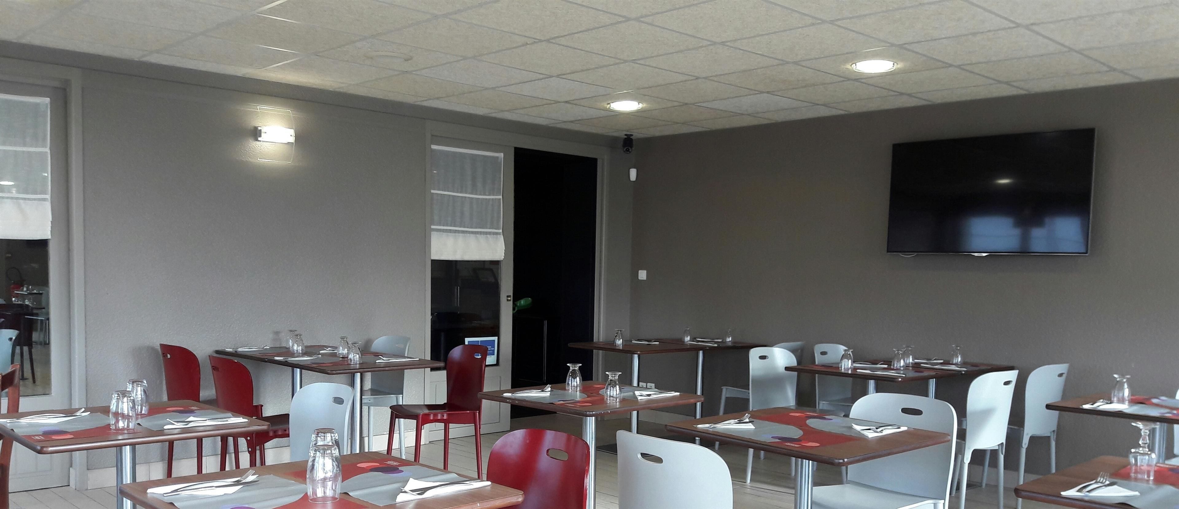 A restaurant with tables and chairs, a flat-screen TV on the wall, and a door leading to another room.