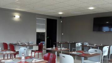 A restaurant with tables and chairs, a flat-screen TV on the wall, and a door leading to another room.
