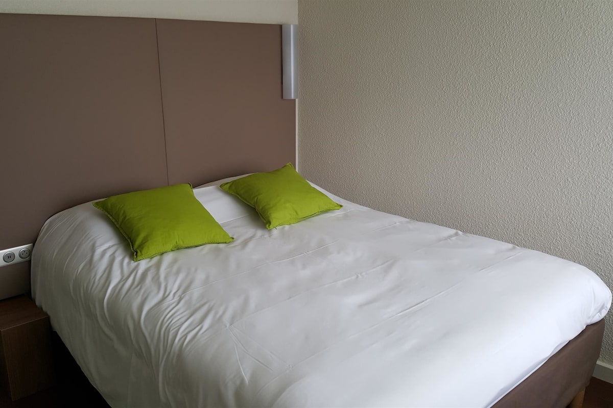 Ein Bett mit weißer Bettwäsche und zwei grünen Kissen, ein braunes Kopfteil und ein kleiner Nachttisch aus Holz.