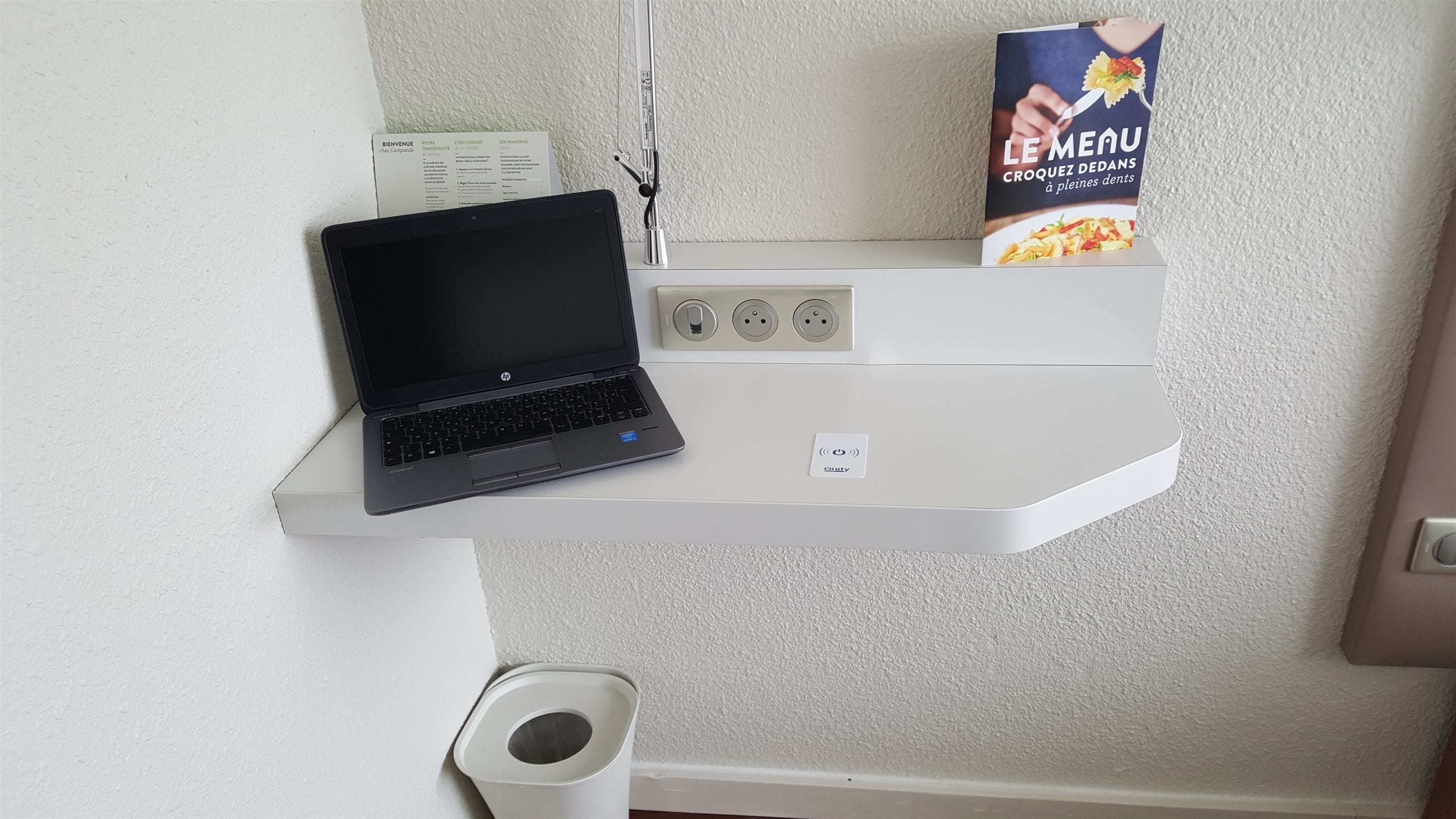 A laptop on a white shelf with a box of croque-monsieur and a menu card.