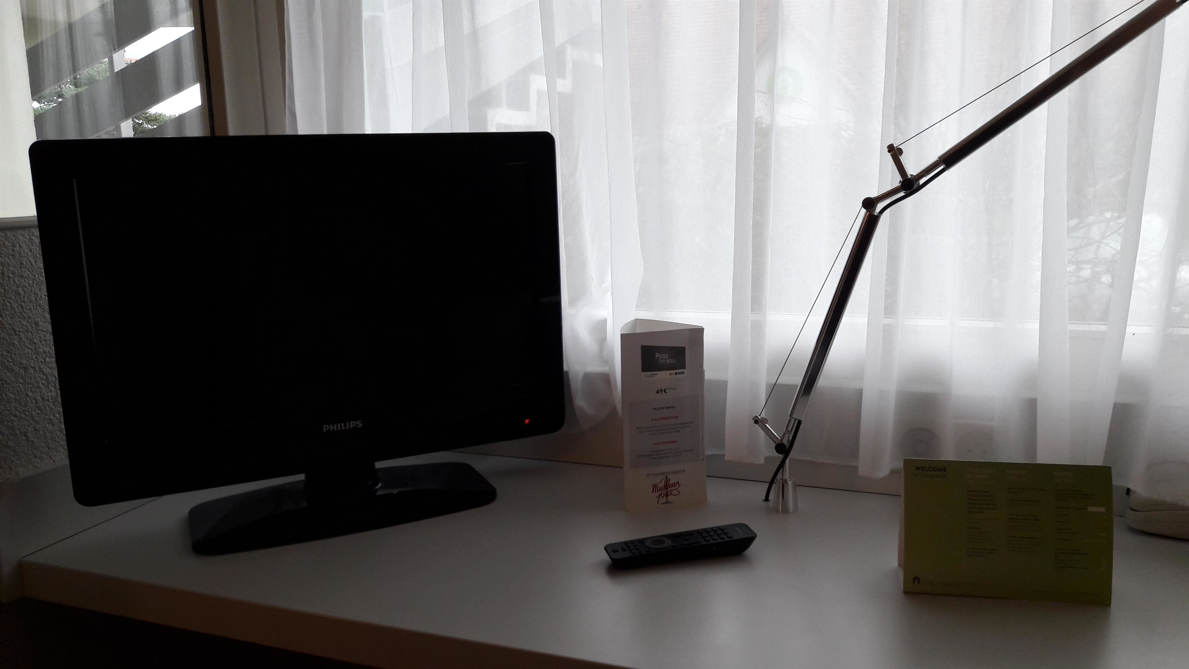 A desk with a Philips monitor, a remote control, a lamp, and a box.