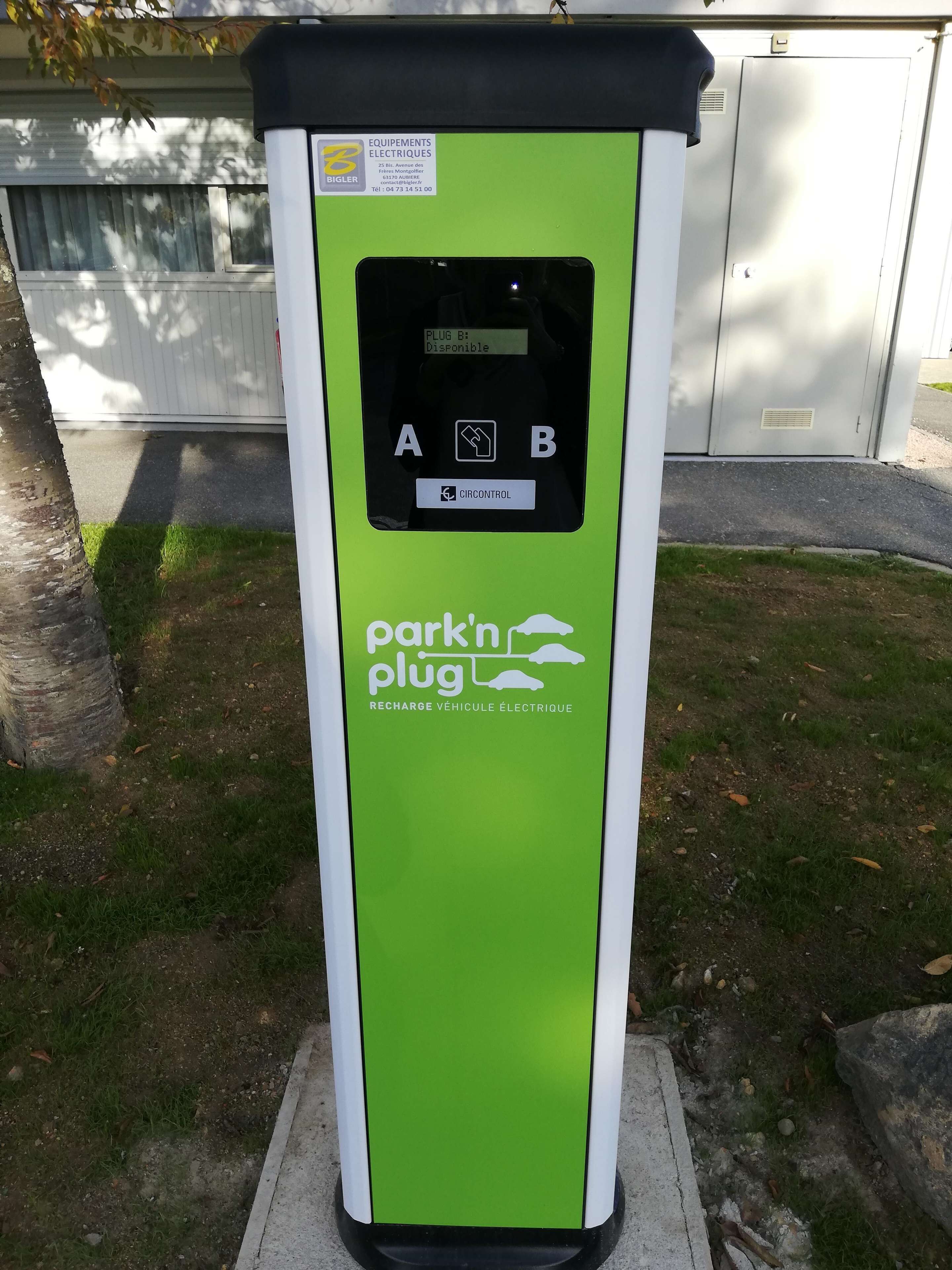 A green and white electric vehicle charging station with a control panel and a sign indicating availability.