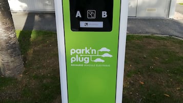 A green and white electric vehicle charging station with a control panel and a sign indicating availability.