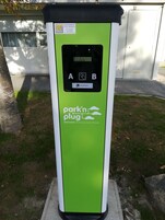 A green and white electric vehicle charging station with a control panel and a sign indicating availability.
