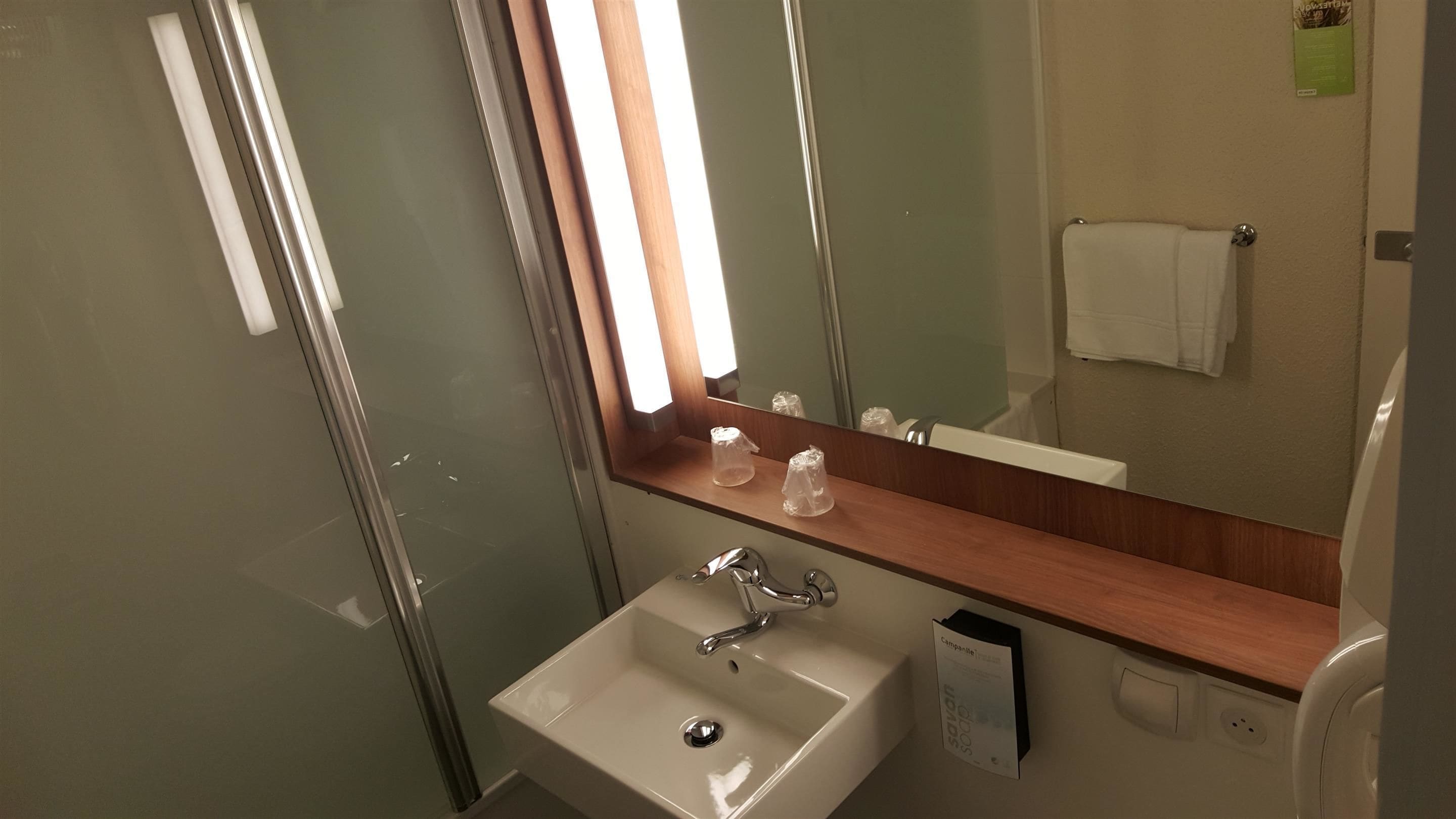Un baño con mampara de vidrio, un lavabo blanco, un espejo y un perchero para toallas.