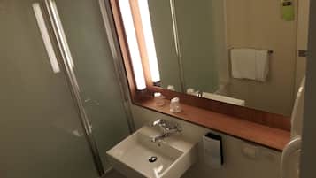Un baño con mampara de vidrio, un lavabo blanco, un espejo y un perchero para toallas.