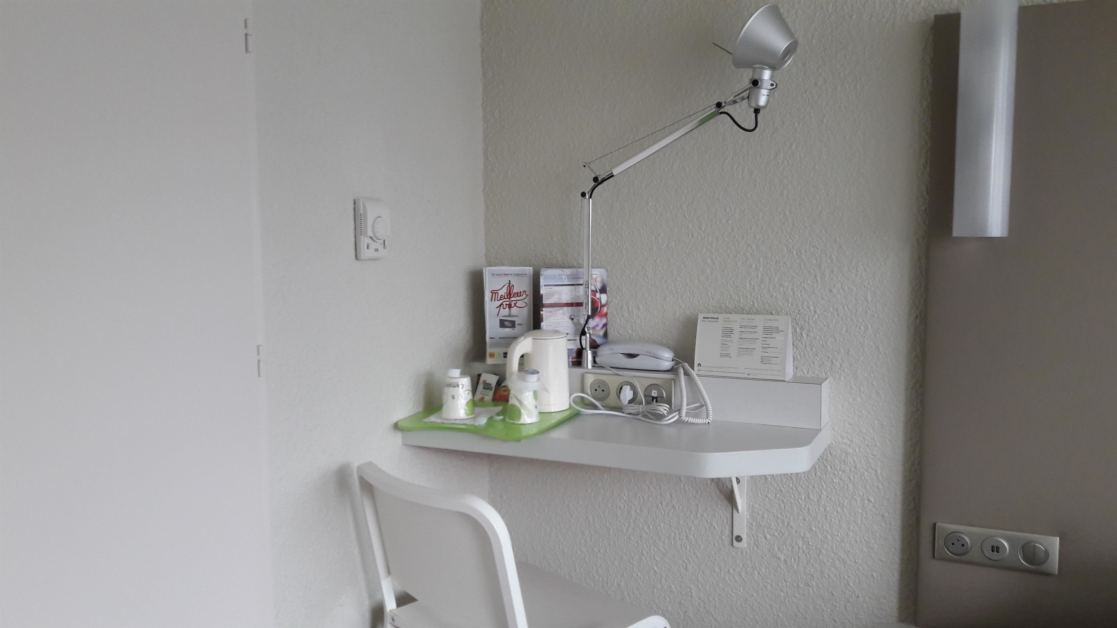 A small workspace with a desk, a chair, a desk lamp, a telephone, and various items on the desk.
