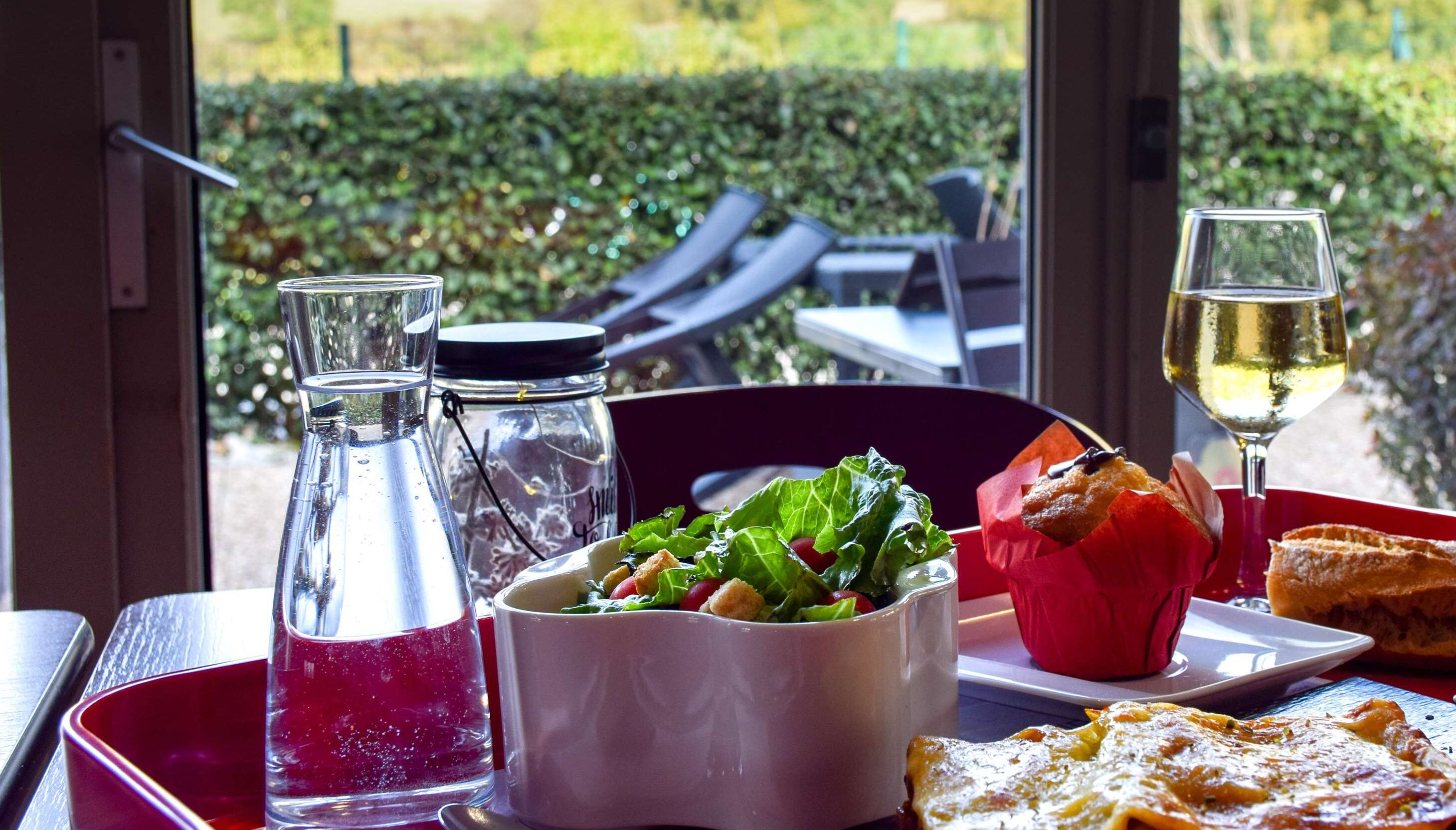 A table with a salad, bread, a glass of white wine, and two bottles of water.