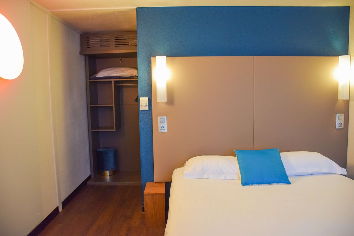 Ein Hotelzimmer mit Etagenbett, Nachttisch, Lampe und blauem Kissen.