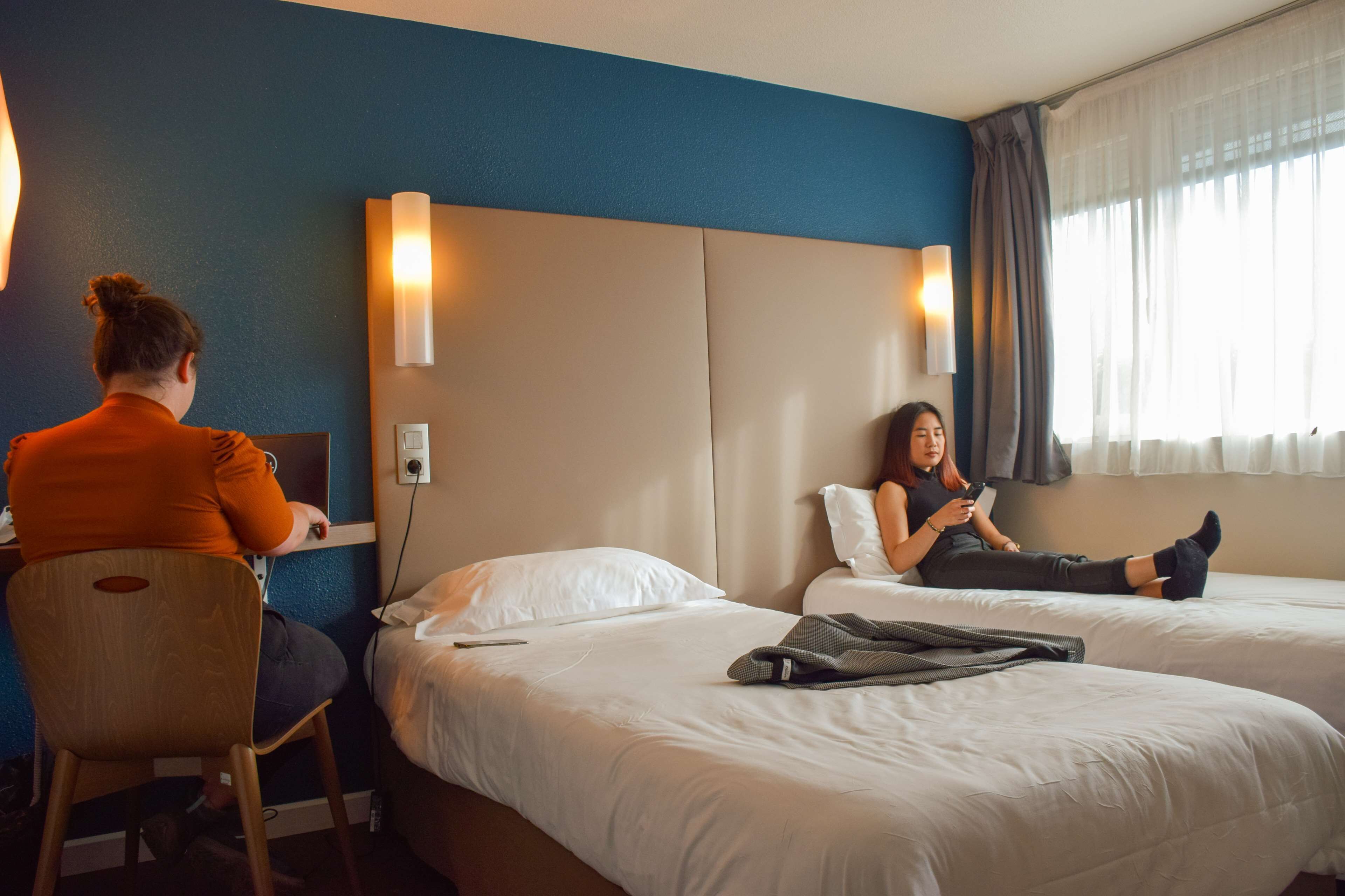 A hotel room with two beds, a desk, and a chair.
