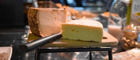 A cheese wheel on a wooden board with a cheese knife beside it.