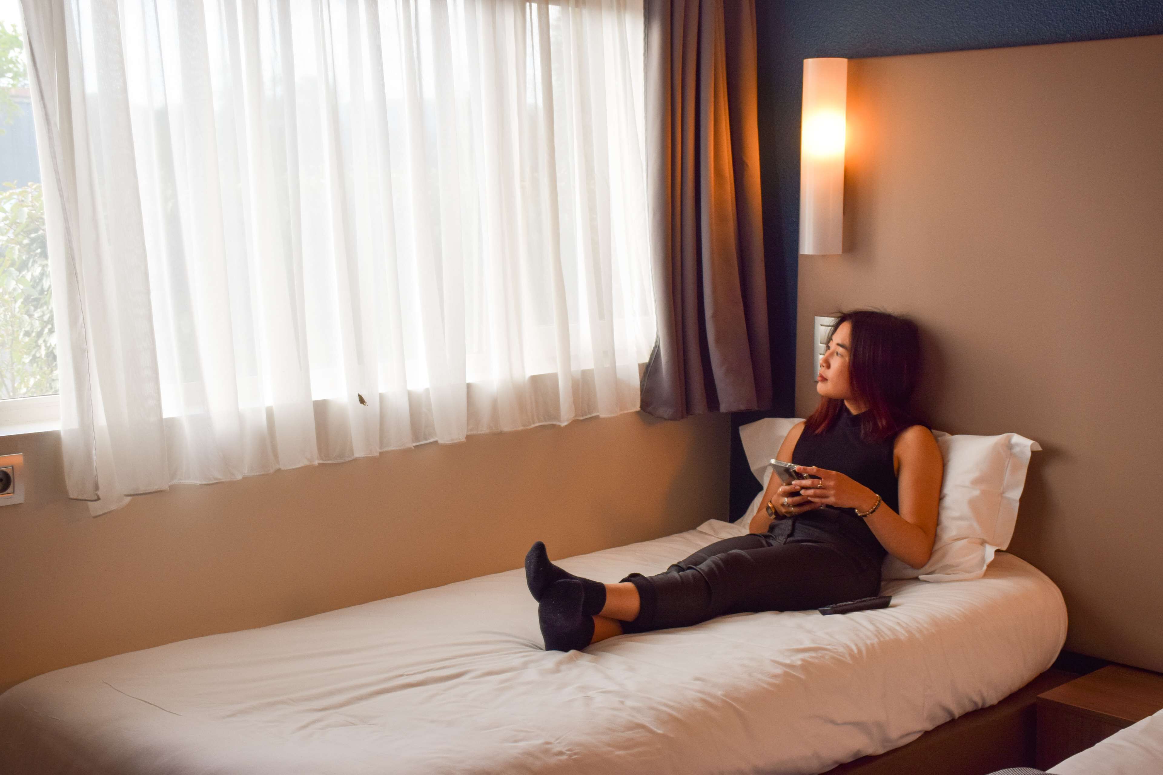 A single bed with white bedding, a bedside table, and a wall-mounted light fixture.