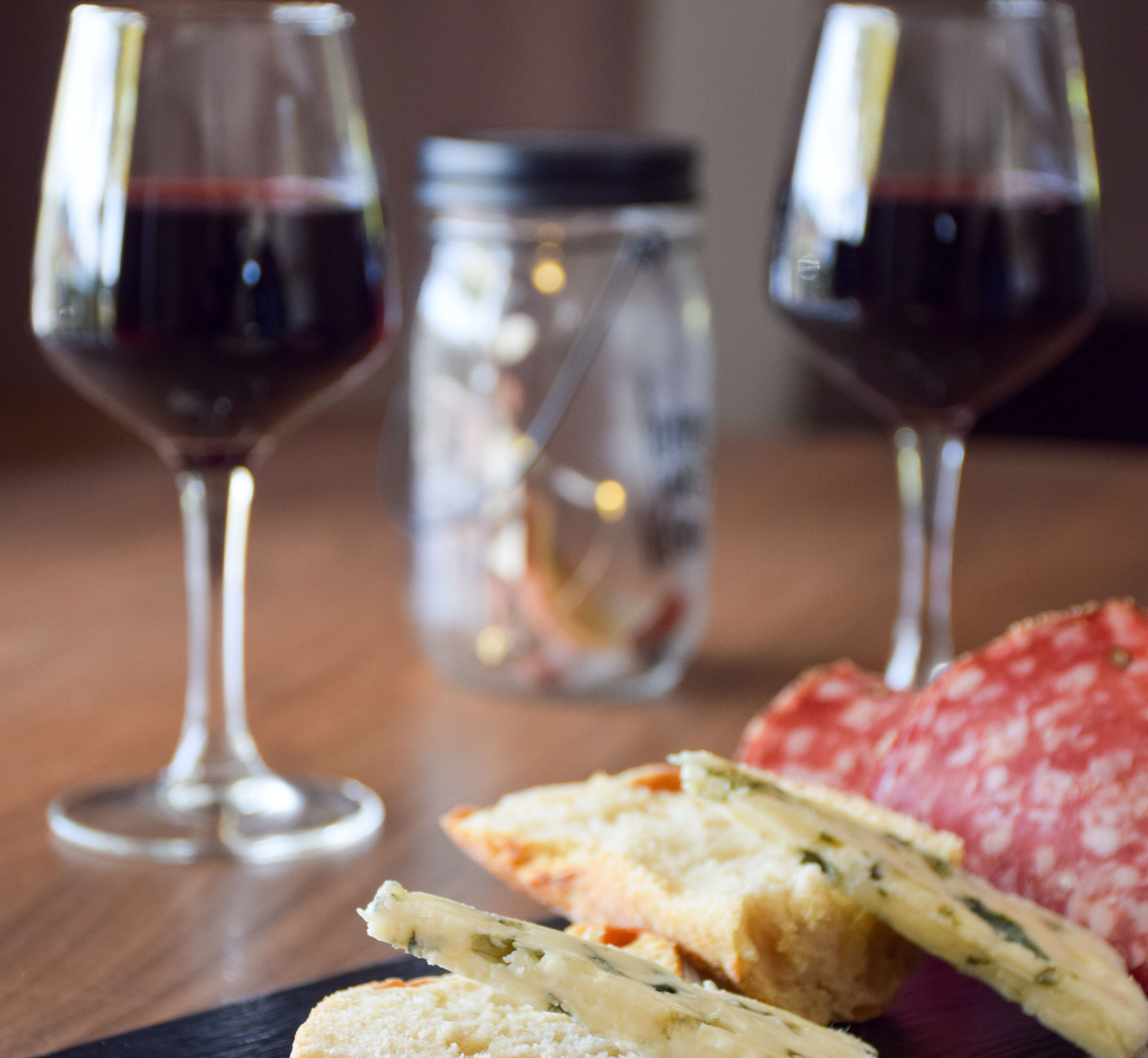 Una mesa de madera con una copa de vino tinto, un tarro, y un plato de pan y salami.