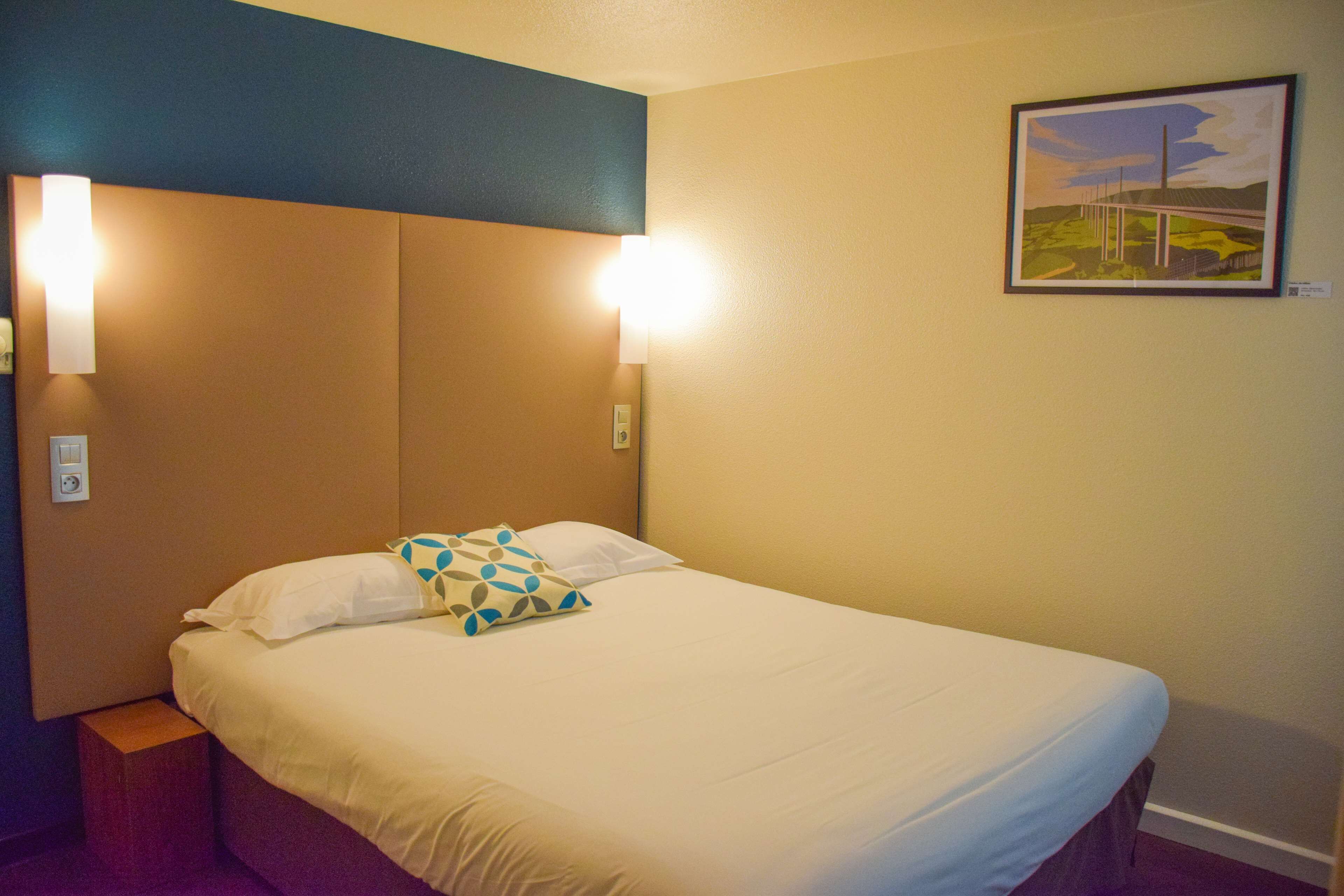 A hotel room with a bed, two wall-mounted lights, and a framed picture on the wall.