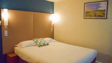 A hotel room with a bed, two wall-mounted lights, and a framed picture on the wall.