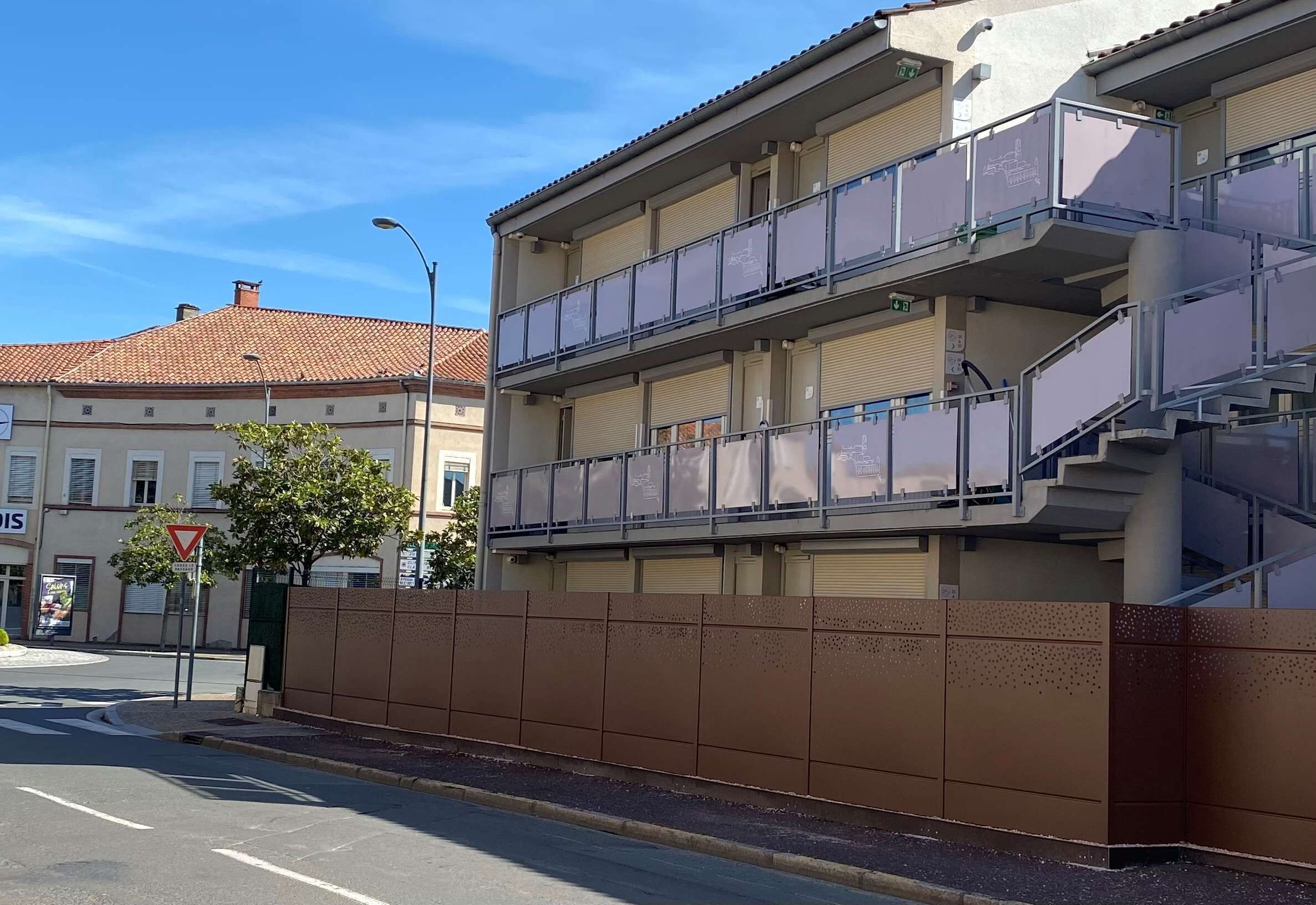 Un edificio de varios pisos con balcones y una pared marrón al frente.