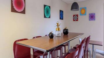 Uma sala de conferências com uma longa mesa de madeira, cadeiras vermelhas e diversas obras de arte abstrata nas paredes.